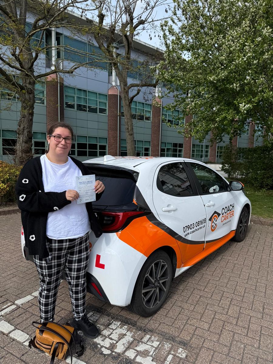 Learner holding her pass certificate next to the CoachCarter car